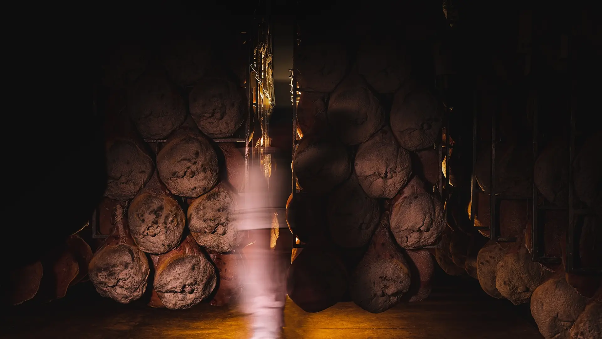 Plusieurs jambons de Bayonne suspendus dans une cave à maturation.